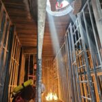 Un sitio estrecho con fuego donde hay un bombero con un casco blanco esperando en el suelo a su compañero.