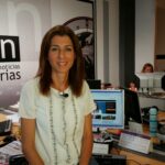 La oficina de antena 3 en canarias donde esta llena de ordenadores y en primera plana esta sentada la periodista Lorena Diaz con una blusa blanca y el pelo por los hombros.