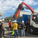 Grupo de operarios con cascos blancos mirando un camión grúa.