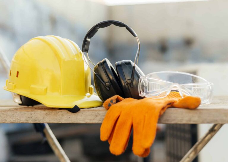 Un casco amarillo, unos guantes naranjas y unos auriculares sobre una mesa de trabajo de una obra